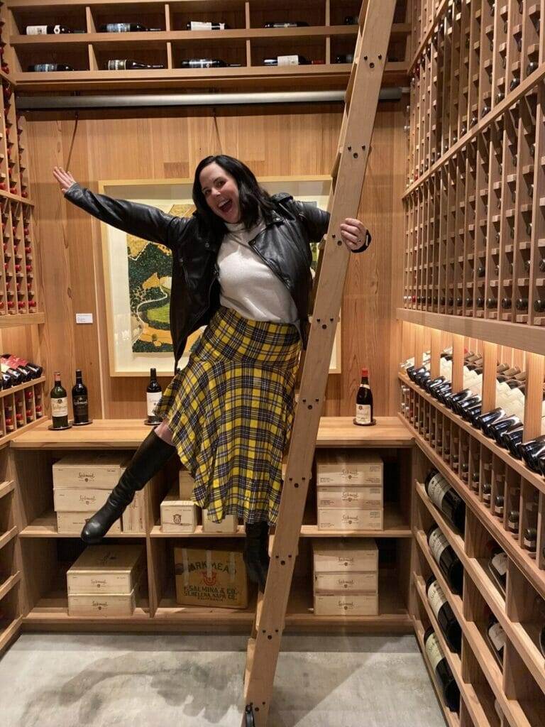 A woman in a home wine cellar, standing on a ladder.