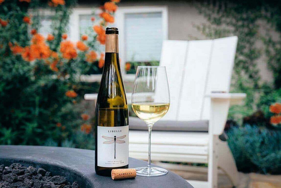 A bottle of white wine sits by a fire pit.