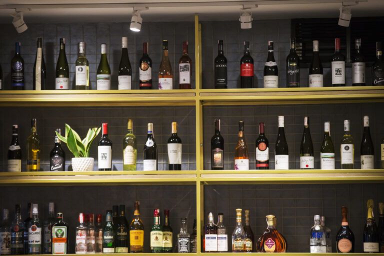 A wine rack displays an assortment of wine and liquor bottles, with the middle shelf holding a potted plant, showcasing unique names on each label.