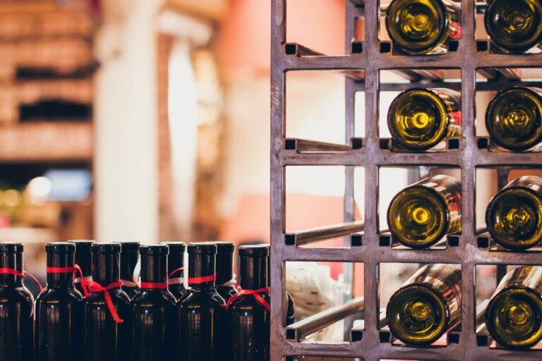 A collection of wine bottles arranged on a store shelf, with a row of standing bottles on the left and racks of horizontally stored bottles on the right showcases cost-effective solutions for wine storage.