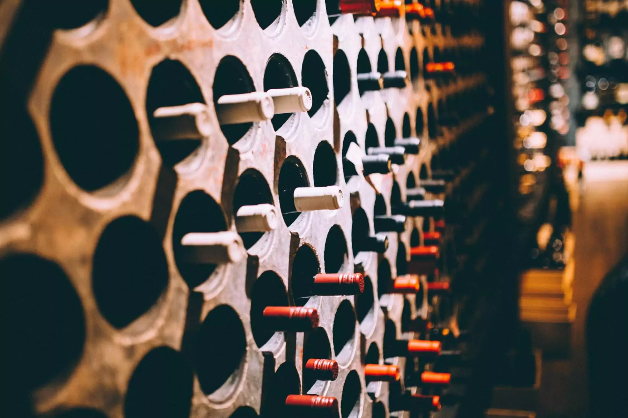 A close-up of wine bottles stored horizontally in a large, circular wine rack, with some bottle caps colored red or white, showcases the efficiency of the Wine Guardian system in maintaining optimal storage conditions.