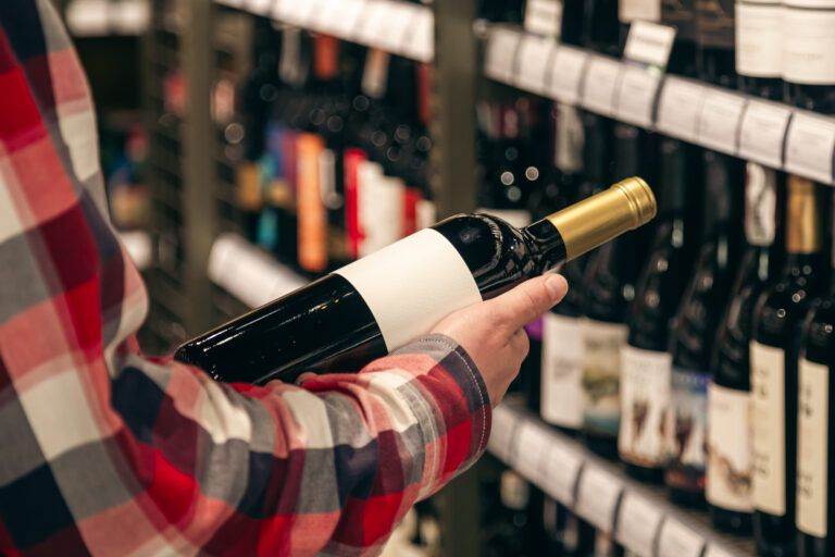 Person in a plaid shirt holding a bottle of wine in a custom wine cellar with shelves stocked with various wines.