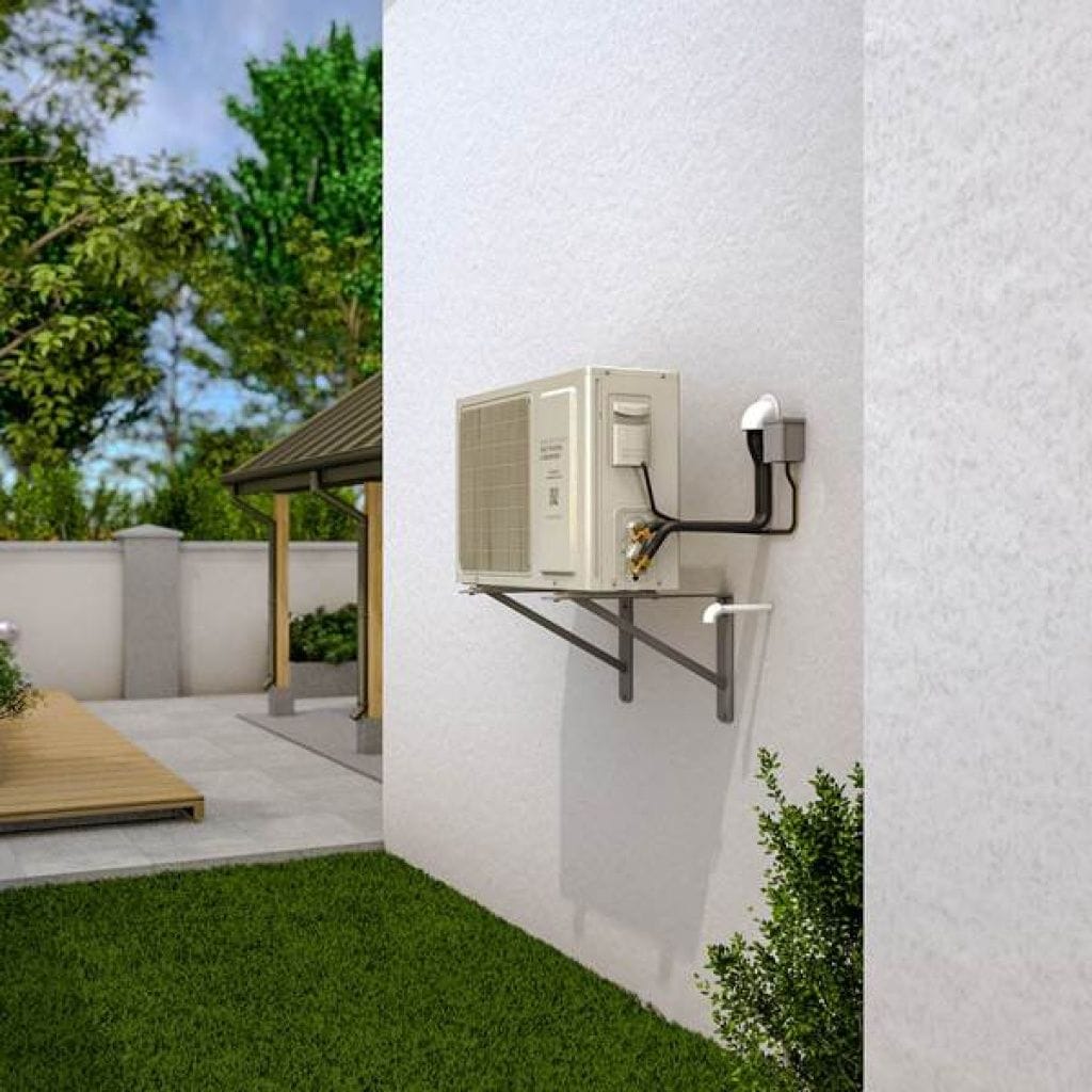 Outdoor air conditioning unit mounted on the exterior wall of a house, next to a green lawn and patio area with a wooden deck and pergola.