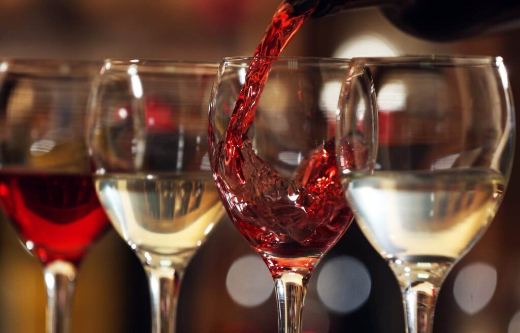 Close-up of red and white wine being poured into four wine glasses, two filled with red wine and two with white wine, against a blurred background; it's as smooth as a Wine Guardian navigating troubleshooting tips.