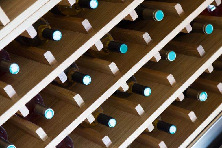 Traditional wine rack holding multiple bottles of wine, viewed from an angle showing the tops of the bottles with blue and gold foil seals.