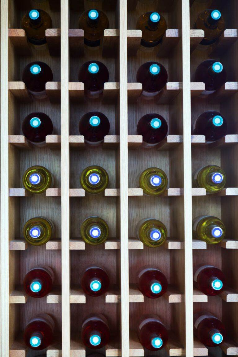 A wooden wine rack holding rows of bottles with dark and light labels, viewed from the bottom, showcasing the circular seals and Wine Hardware.