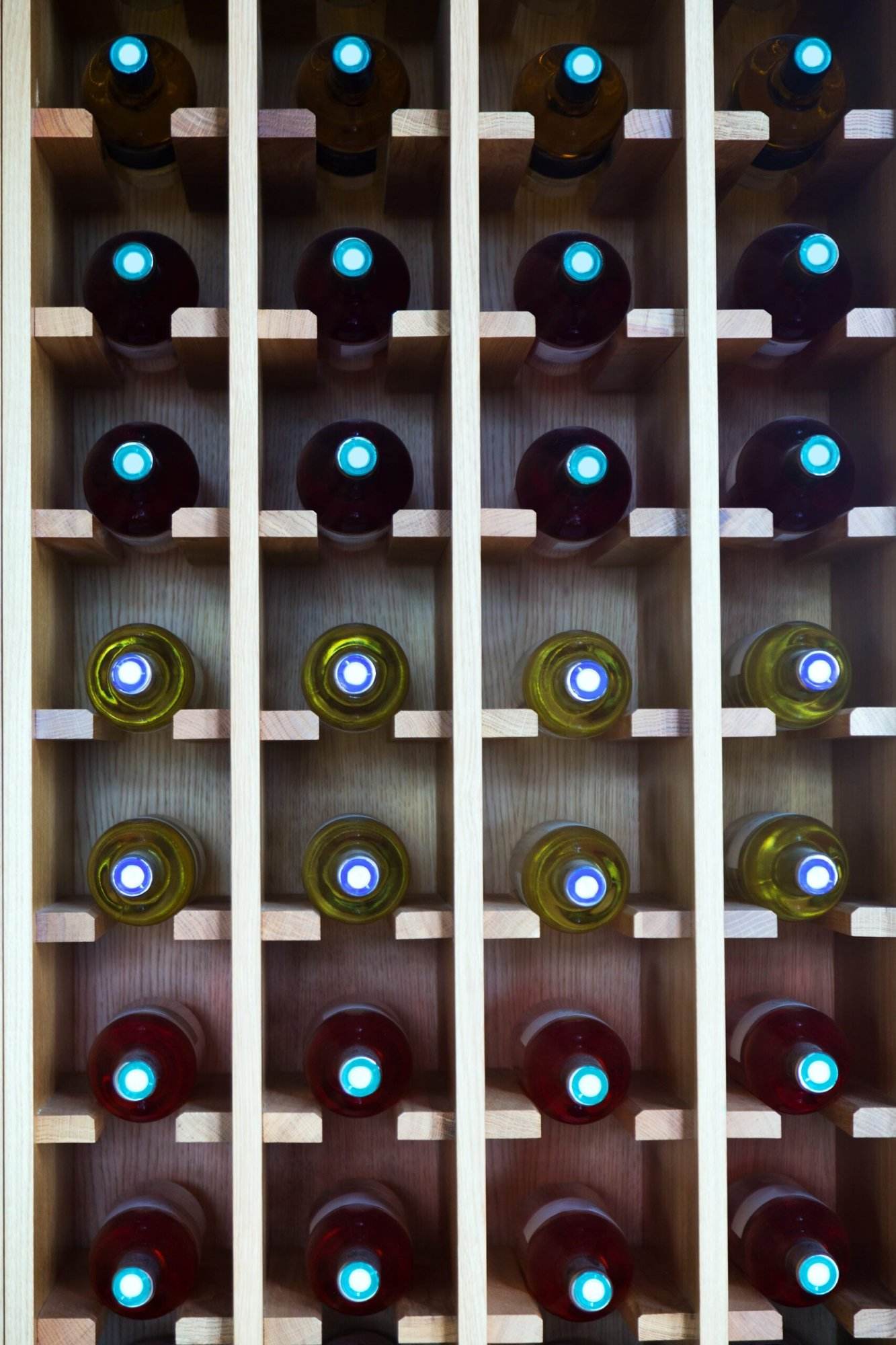 A wooden wine rack holding rows of bottles with dark and light labels, viewed from the bottom, showcasing the circular seals and Wine Hardware.