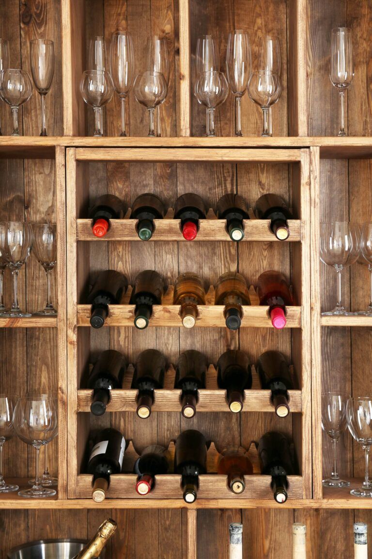 A wooden wine rack features a central section with three rows for various wine bottles, and surrounding sections for empty wine glasses. For those considering the cost to build, this elegant piece embodies both functionality and style.