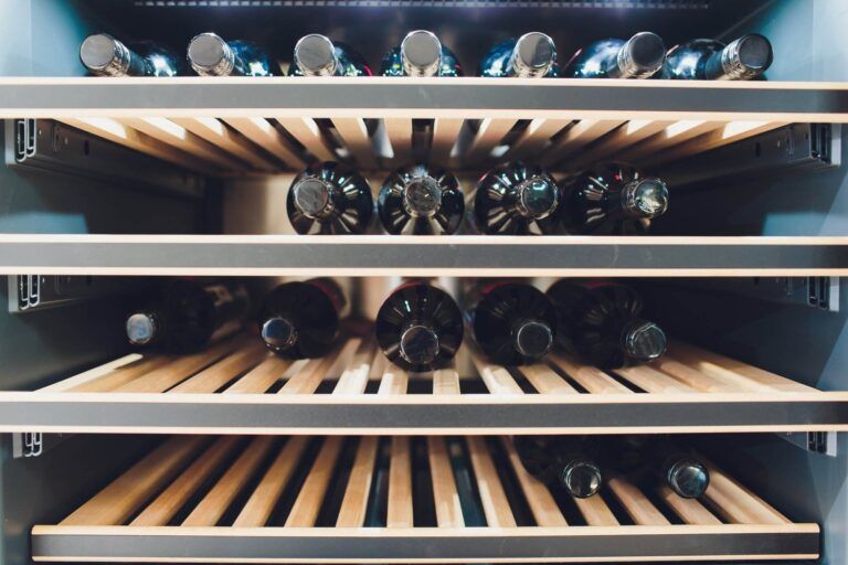 A wine refrigerator with wooden shelves holding several bottles—both upright and lying on their sides—offers the perfect storage solution. Available in both single-zone and dual-zone options to suit your collection's needs.