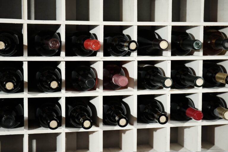 A wine rack filled with various bottles, each slot holding an individual wine bottle, mostly with dark-colored labels and several with red and white caps. This exquisite piece of wine hardware adds a touch of elegance to any space.