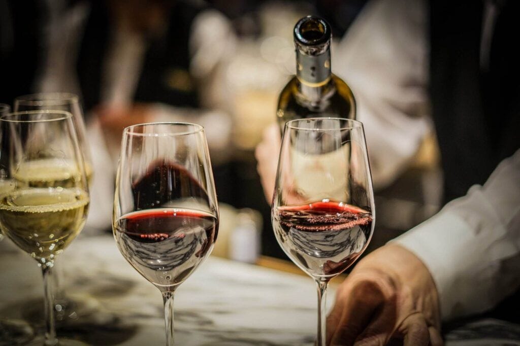 A bartender pours wine into glasses; two glasses contain red wine while one has white wine. For home wine storage, consider using a space-saving wine rack to keep your bottles organized and accessible.