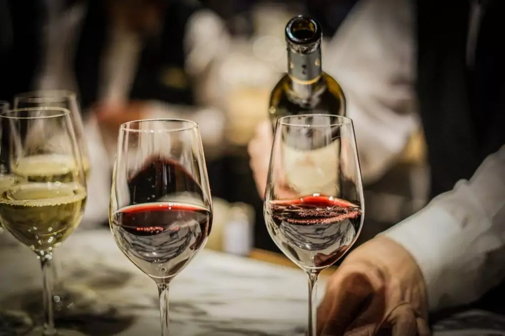 A bartender pours wine into glasses; two glasses contain red wine while one has white wine. For home wine storage, consider using a space-saving wine rack to keep your bottles organized and accessible.