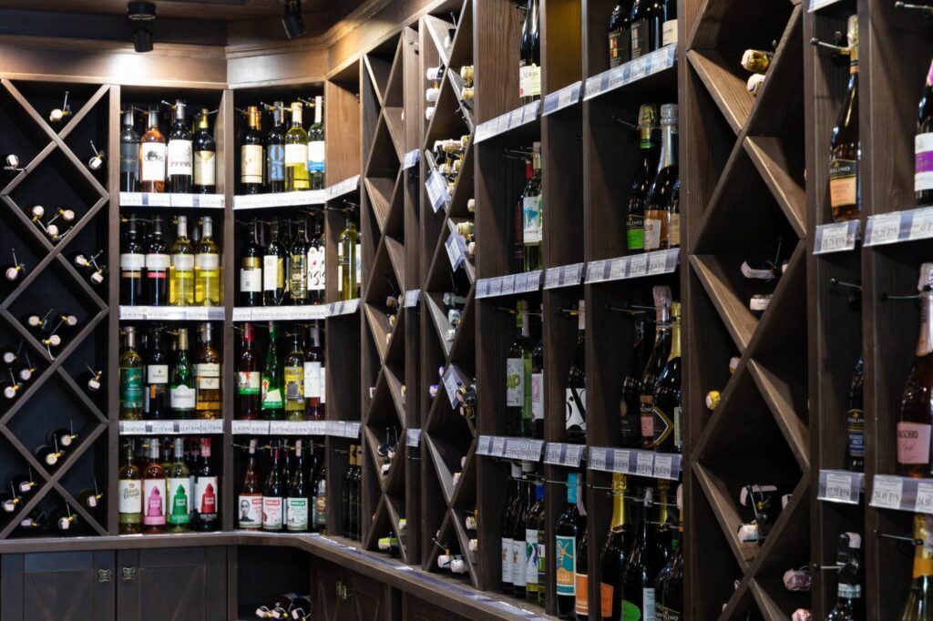 A wine store shelf boasts a variety of wine bottles organized in diamond-shaped wine racks, with price tags visible underneath some of the bottles, providing both elegance and space-saving tips for choosing the right size rack.