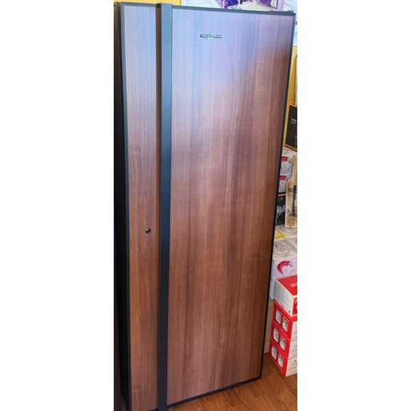 A Transtherm Artevino Oxygen Solid Door refrigerator with a wood-patterned finish and vertical black handle stands in a room with boxed items nearby.