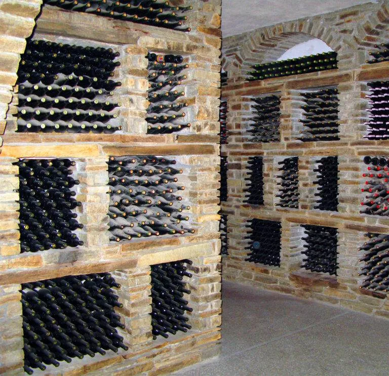 A wine cellar designed by renowned architects in Walnut Creek, featuring stone walls and shelves filled with numerous bottles of wine arranged horizontally.