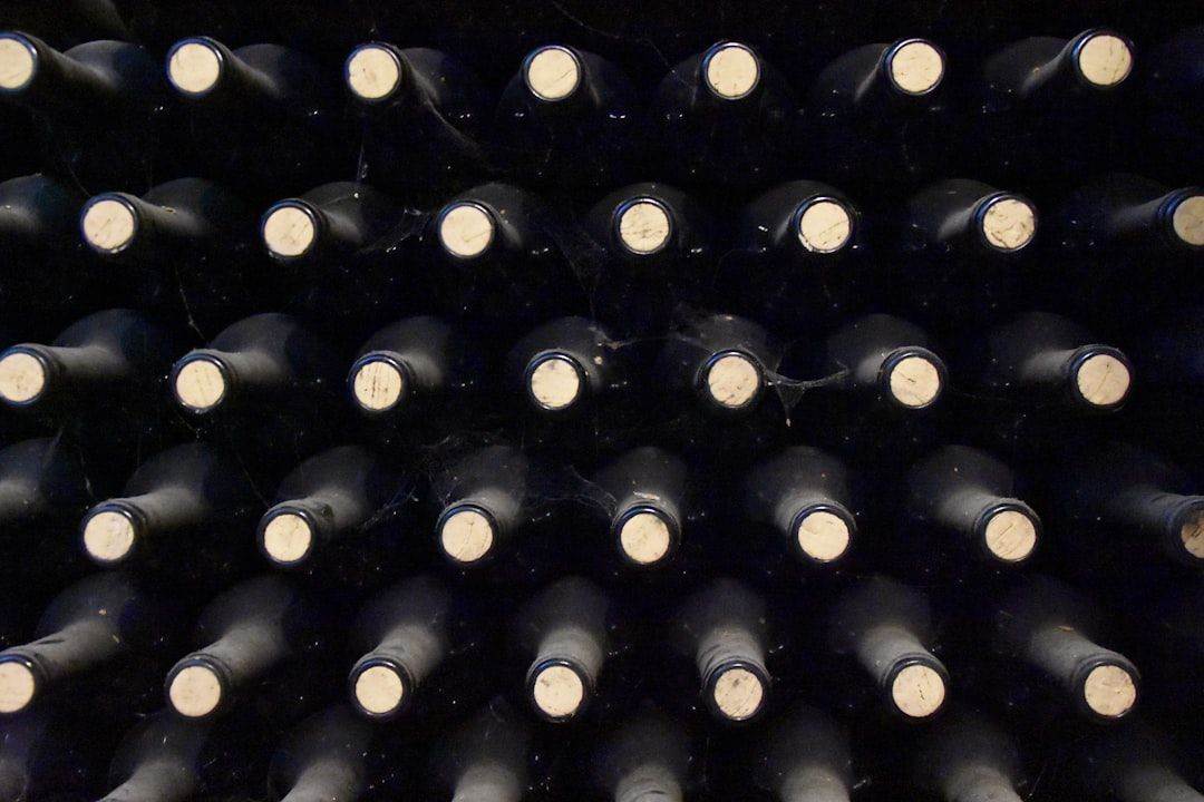 A close-up view of rows of wine bottles stored horizontally in a dark cellar, with corks facing outward.