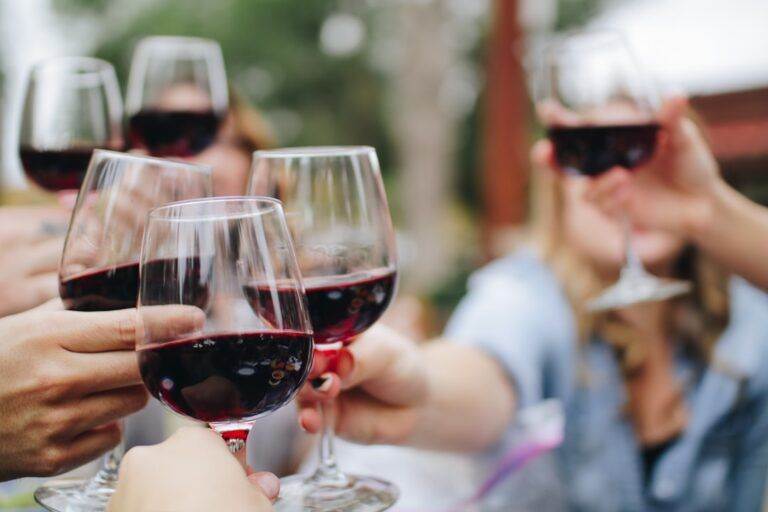 People clinking wine glasses filled with red wine in an outdoor setting.