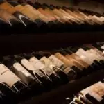 Rows of wine bottles are stored horizontally on shelves in a dimly lit cellar.