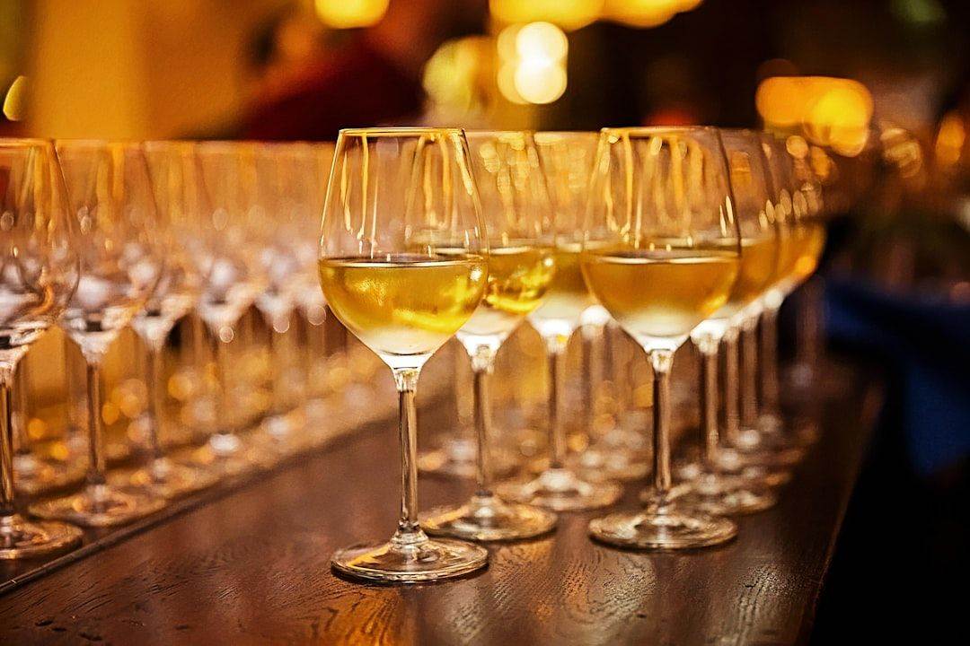 Rows of wine glasses filled with white wine are lined up on a wooden table in a dimly lit setting.