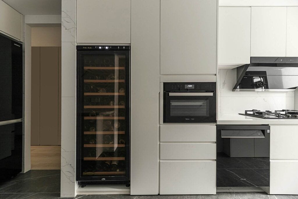 Modern Danville kitchen featuring a wine cooler, oven, stovetop, and sleek white cabinetry. The black and white color scheme with marble accents complements the elegance of wine refrigerators. .