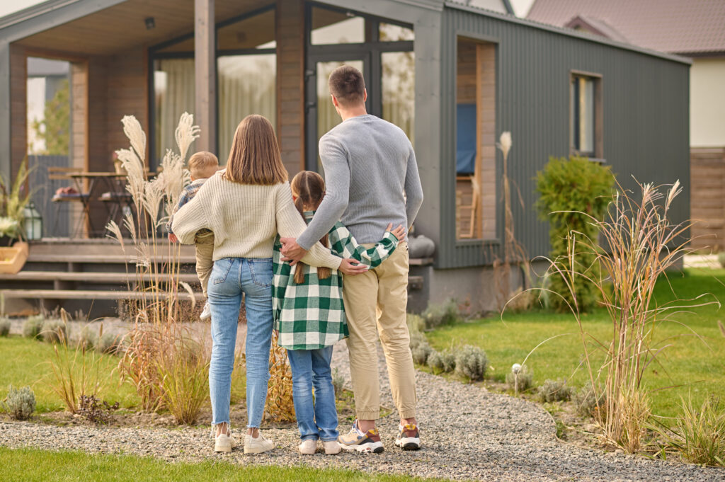 A family of four stands on a stone path outside a modern house, facing away from the camera and admiring their Tahoe vacation home together.