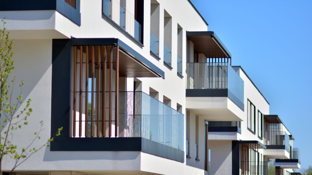 Modern San Francisco apartments featuring glass balconies, wooden slats, steel studs, and white exterior walls under a clear blue sky.