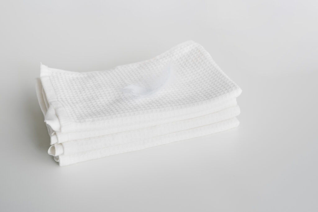 A stack of folded white waffle-weave towels with a small white feather resting on top, placed on a plain white surface—ideal for spaces with low humidity or to help manage cellar moisture.