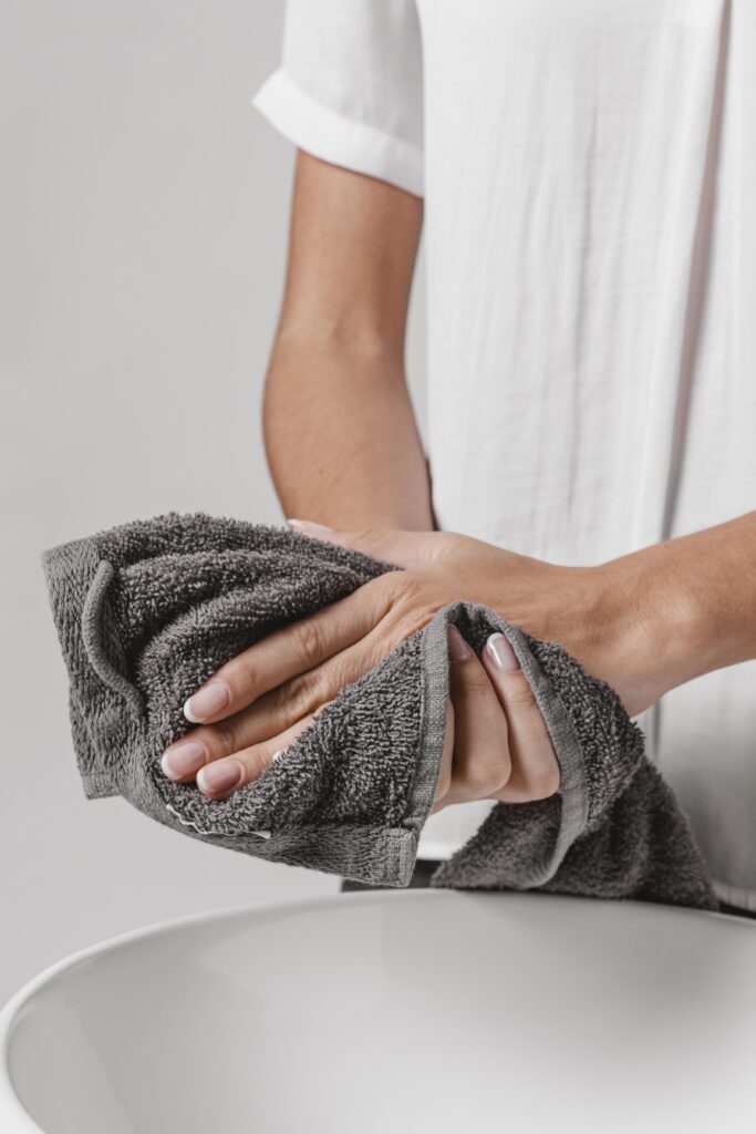 A person drying their hands with a dark gray towel over a white basin, mindful of cellar humidity that can affect how towels dry.