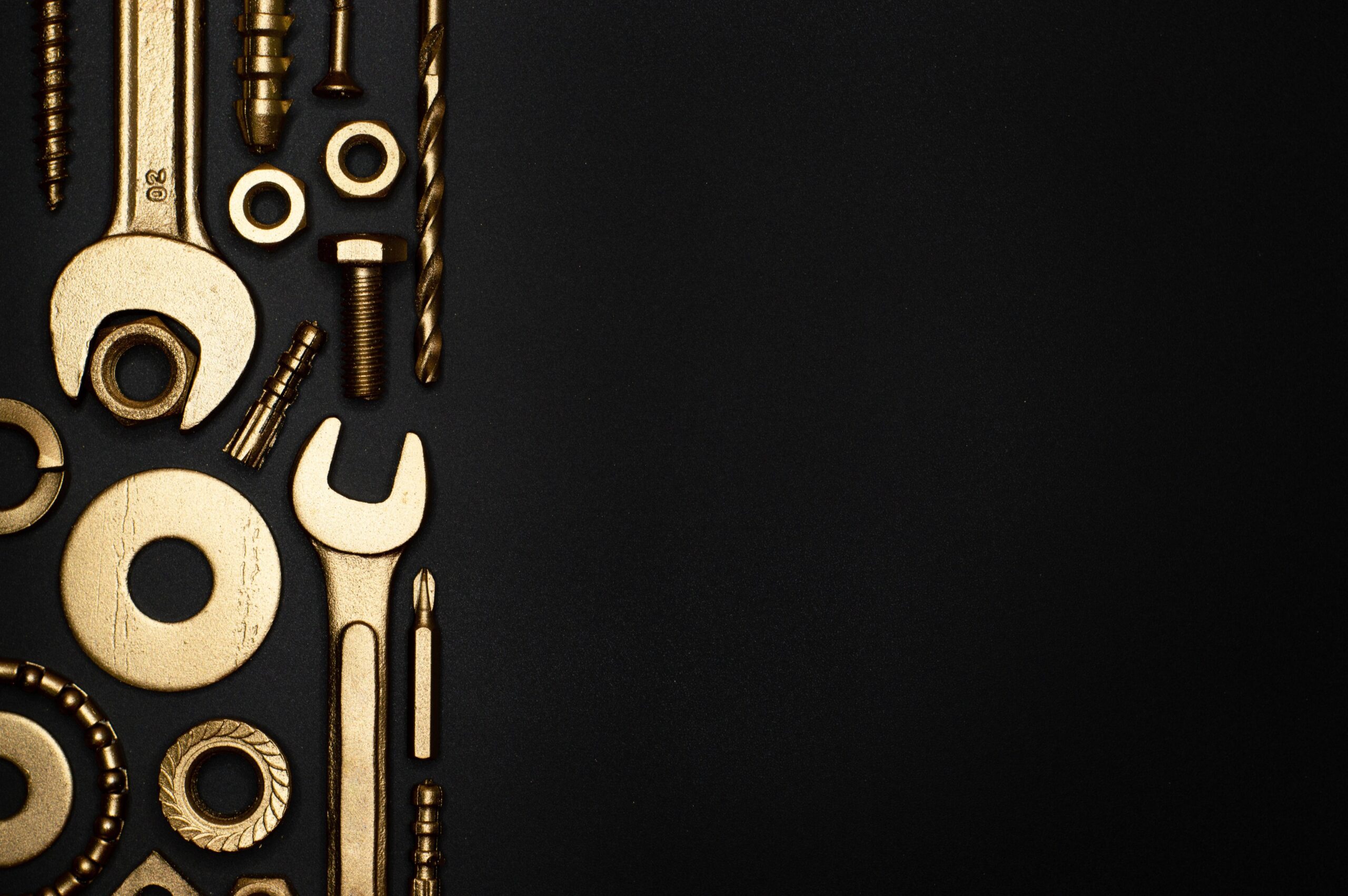Assorted gold-colored tools and hardware, including wrenches, screws, bolts, and washers—perfect for work on San Francisco apartments—arranged vertically on the left side against a black background.