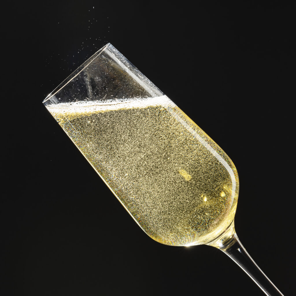 A close-up of a tilted champagne flute filled with sparkling wine against a black background, inspired by elegant Champagne bottles found in exclusive Napa collections.