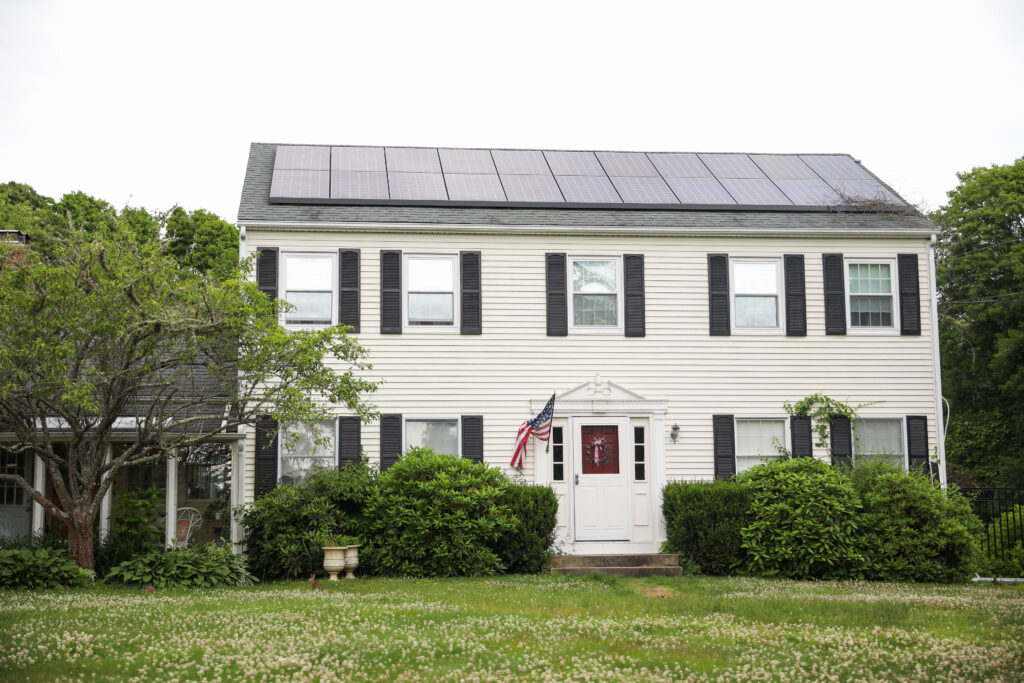 Two-story house with cream siding, black shutters, solar panels on the roof, an American flag by the door, a wine cellar, and green bushes in the front yard—a beautiful example of Sonoma County solar-powered homes.