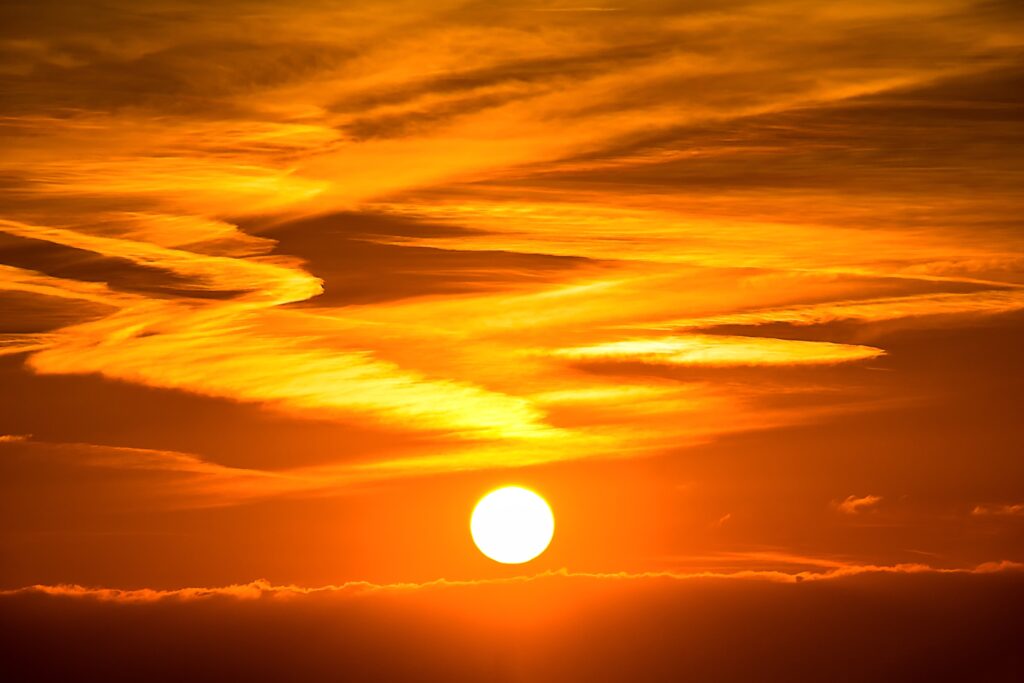 The sun is setting below a layer of clouds in Northern California, with orange and yellow streaks filling the sky after a day marked by heat waves.