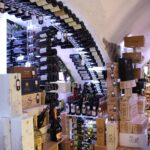 Wine cellar with arched racks holding bottles, surrounded by stacked wooden wine crates and boxes under a vaulted ceiling—ideal for proper cellar humidity and easy cellar maintenance.