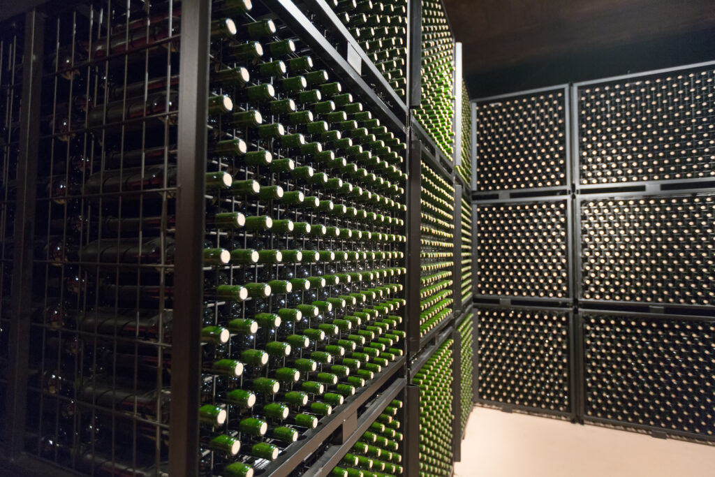 Rows of wine bottles are stacked horizontally on metal racks in a wine cellar, with the bottle necks facing outward—a setup that benefits from wine cooler compressors designed to withstand coastal air corrosion.