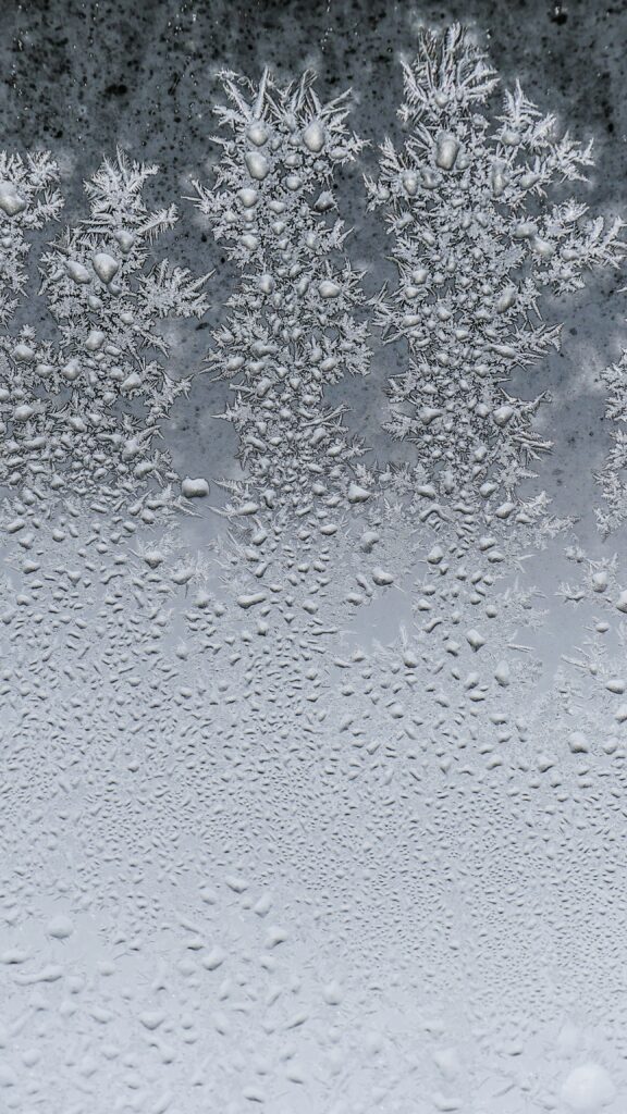 Close-up of frost crystals and condensation forming intricate patterns on a windowpane.
