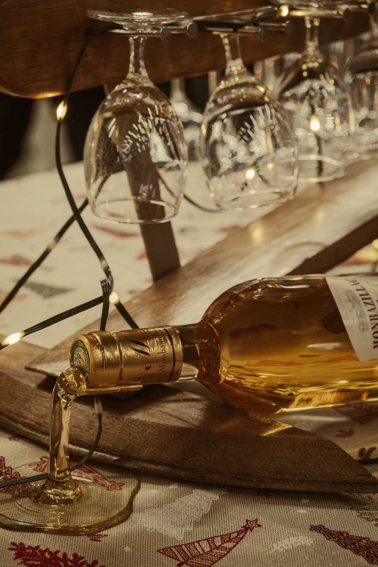 A bottle of white wine elegantly pouring into a glass surrounded by hanging wine glasses and warm lighting.