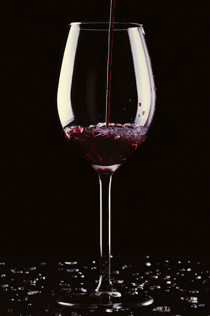 Close-up of red wine being poured into a clear crystal glass against a black background.