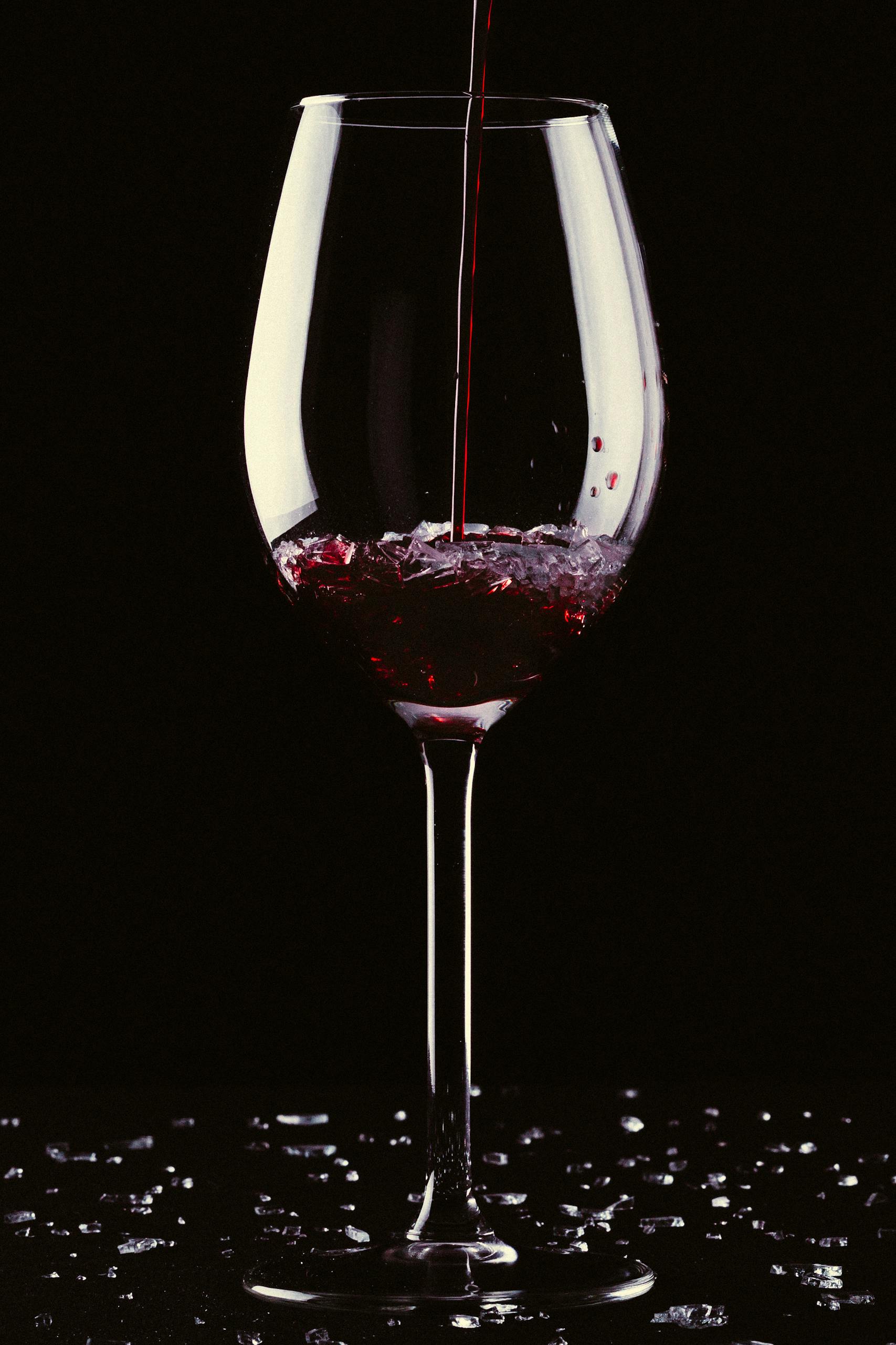 Close-up of red wine being poured into a clear crystal glass against a black background.