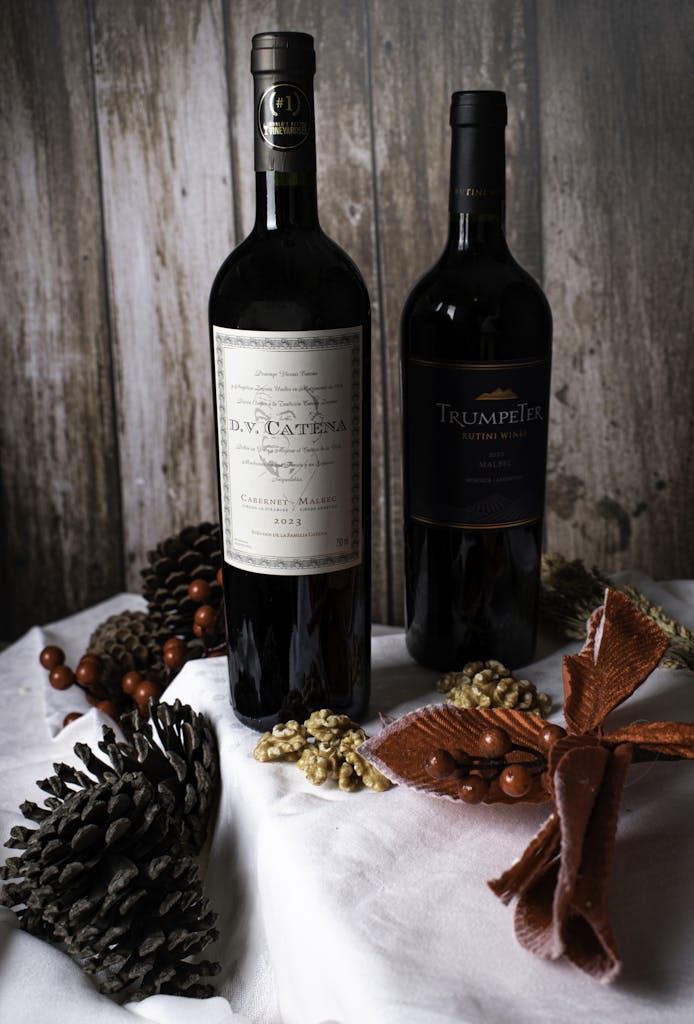 Two bottles of wine with festive decorations, pinecones, and walnuts on a wooden backdrop.