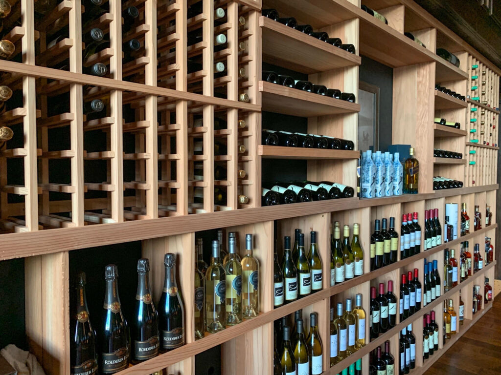 Wooden shelves filled with bottles of wine, sparkling wine, and bottled water line this commercial wine cellar, all organized in rows for optimal wine storage in a sophisticated tasting room.