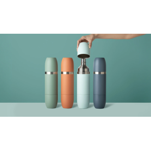 Four matte bottles—including the High Camp Parkside Flask™ 750 with two magnetic tumblers—stand in a row; a hand lifts a tumbler from the light blue flask, revealing its insulated metal interior.
