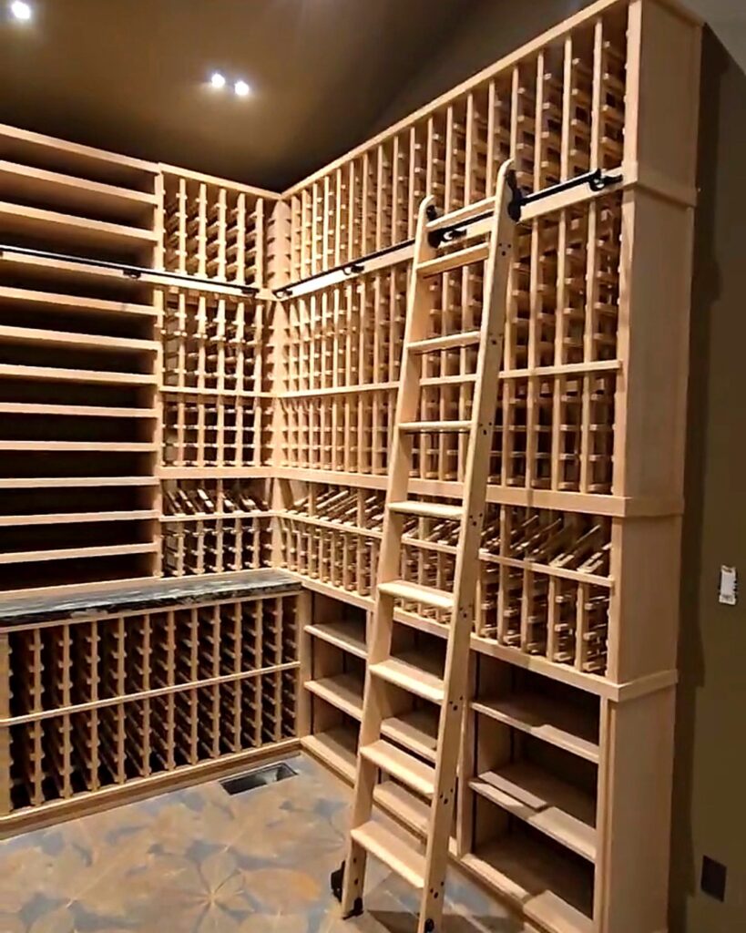 Custom wine cellar with floor-to-ceiling wood wine racking, rolling ladder, and integrated display shelves by Wine Hardware.